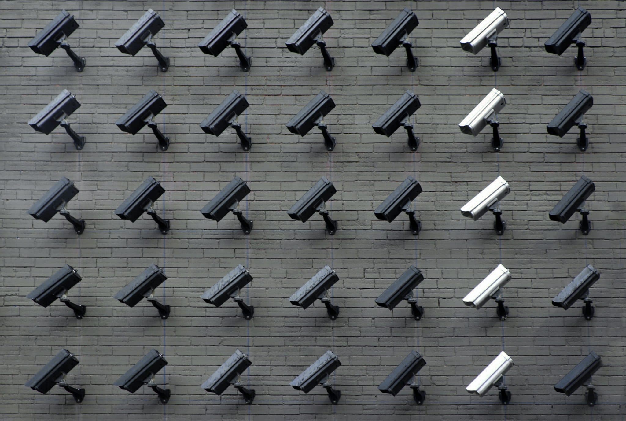 A grid of surveillance cameras mounted on a grey brick wall