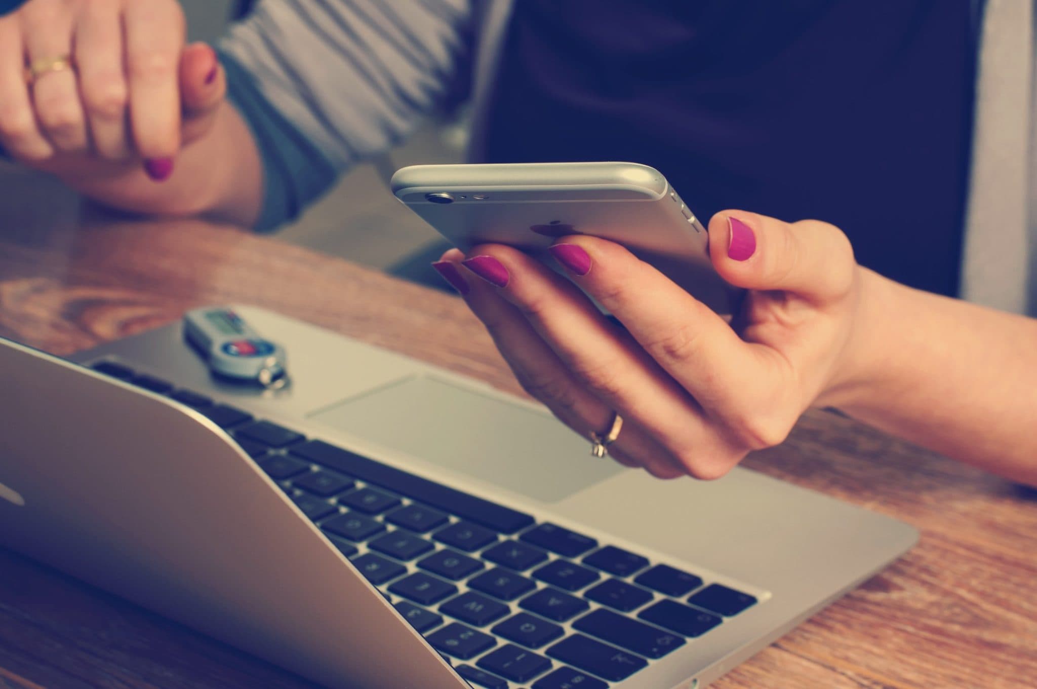 A woman holding a phone in one hand while working at a laptop