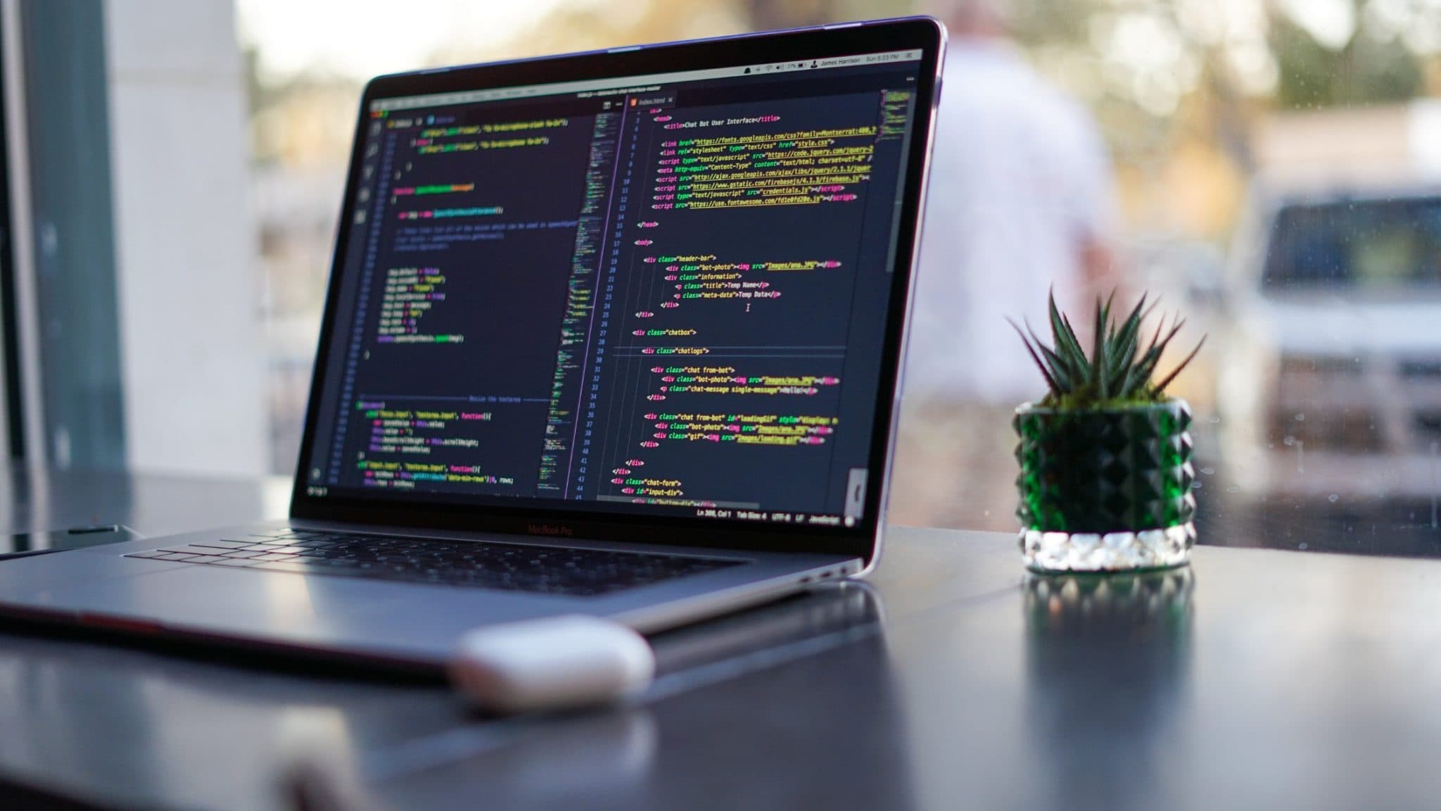 A laptop showing source code on a desk beside a potted cactus